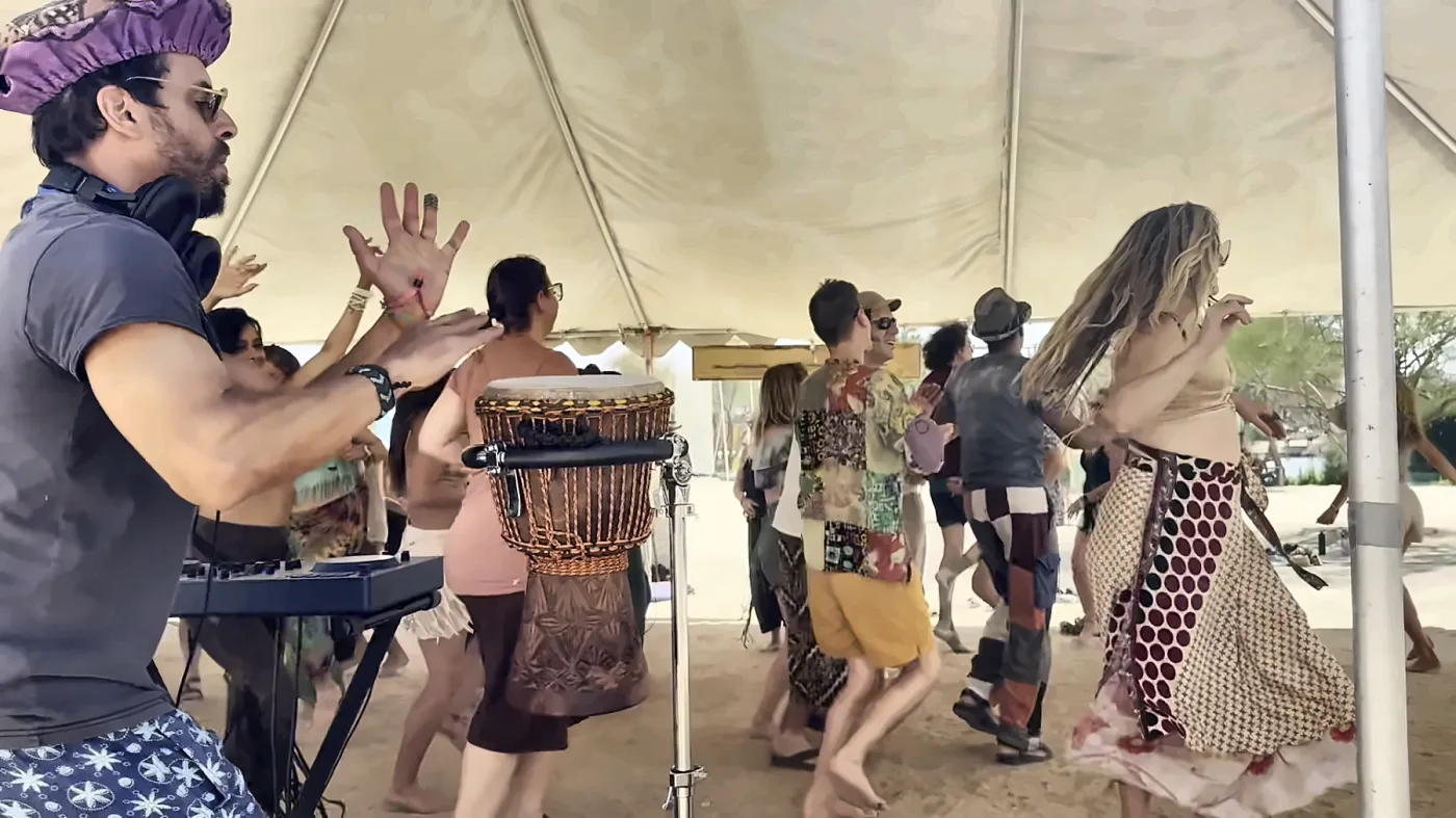 Taïb with his hands up behind the djembe at a daytime party