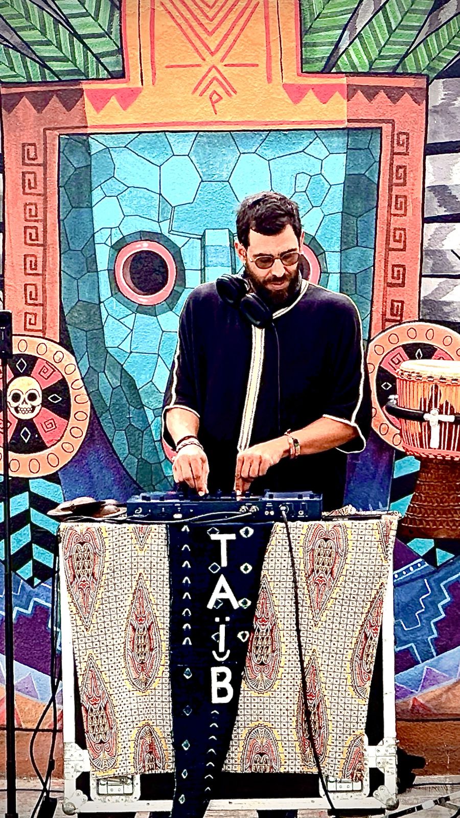 Taïb DJing in front of a painted mural